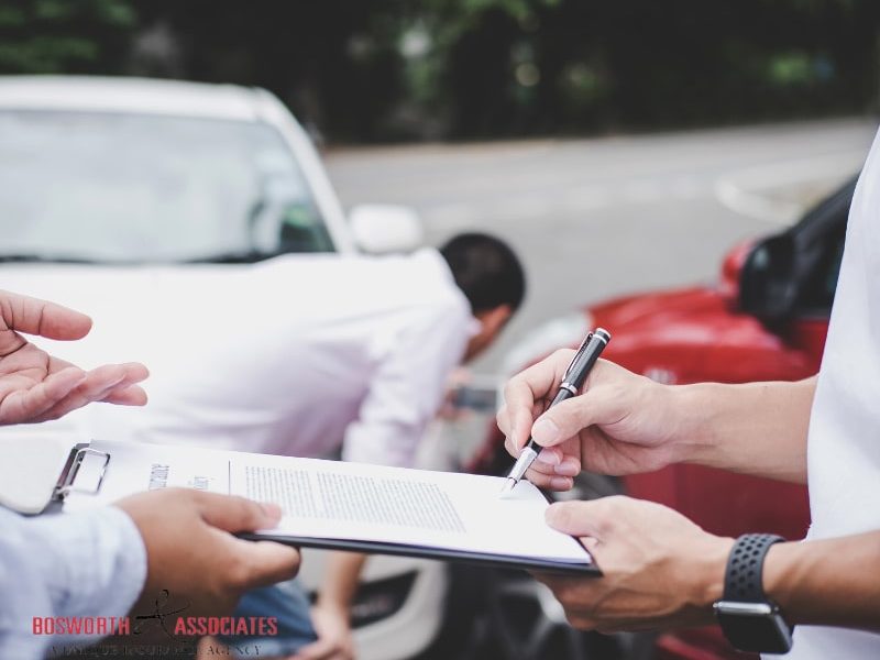 An insurance agent examines the damaged car, and the customer files a signature on the auto insurance form.