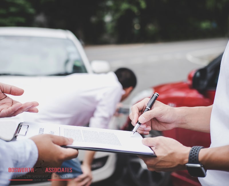 An insurance agent examines the damaged car, and the customer files a signature on the auto insurance form.