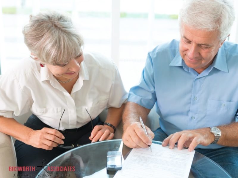 An elderly couple reading a life insurance plan and signing a life insurance form.