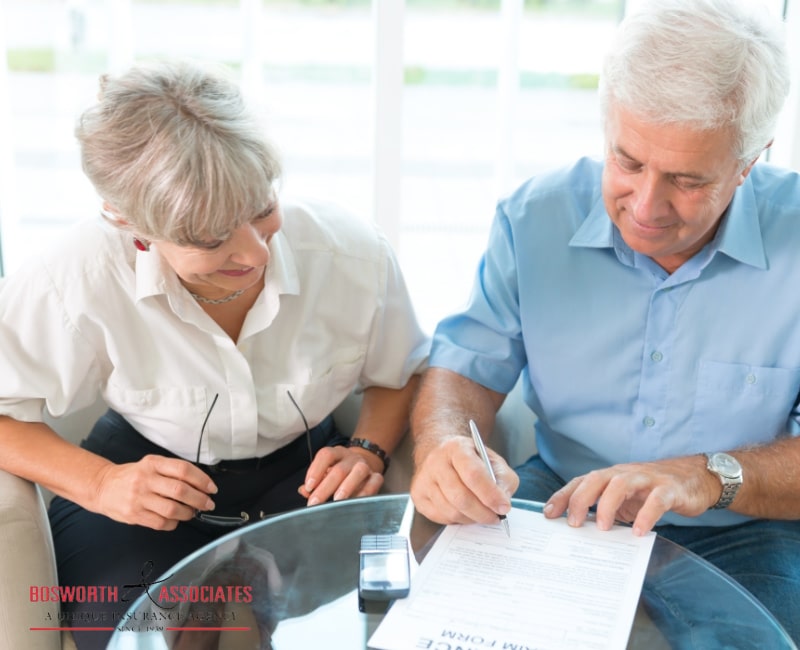 An elderly couple reading a life insurance plan and signing a life insurance form.