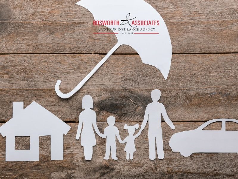 Paper silhouettes of a house, family, and a car under an umbrella symbolizing an umbrella insurance policy.