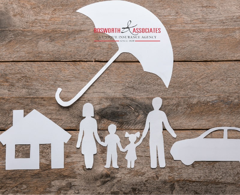 Paper silhouettes of a house, family, and a car under an umbrella symbolizing an umbrella insurance policy.