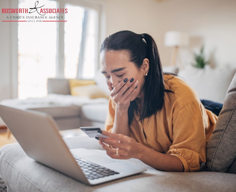 A woman in a yellow t-shirt holding her card in front of the laptop, looking upset. Possible victim of an insurance scam.